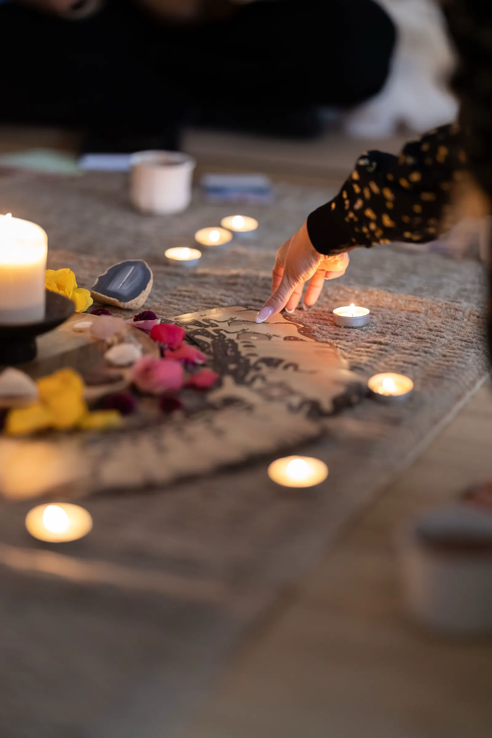 A hand choosing an oracle card beside candles and petals.